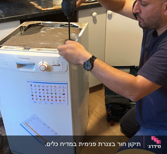 אדם מתקן מדיח כלים עם מברגה חשמלית
